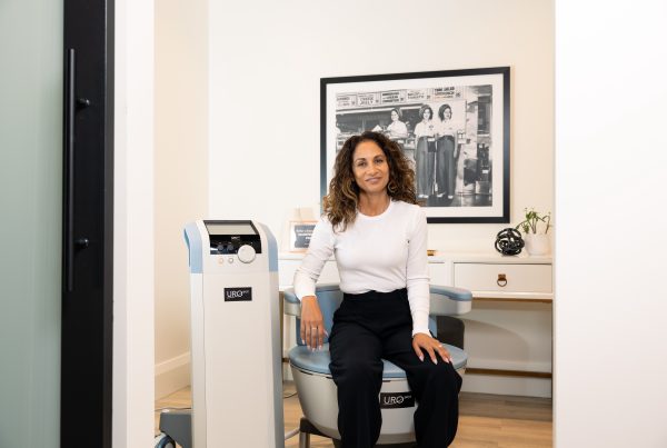 women in white top and black pants sitting on emsella chair at Urospot.